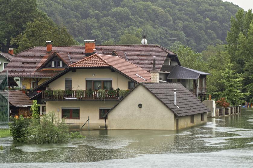  Flooded water flowing through river surrounded by houses in village. 