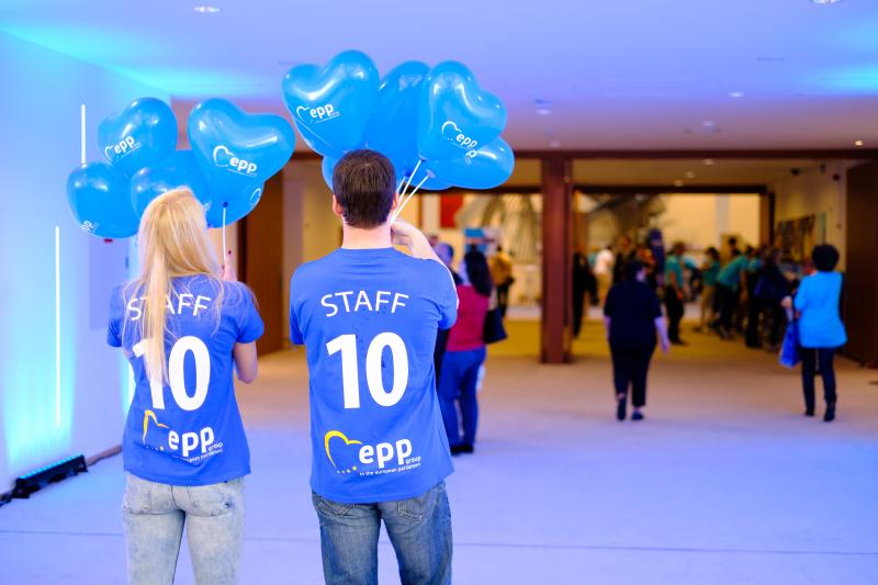 2 members of staff wearing 'Staff' t-shirts hold EPP Group balloons at the Parliament Open Days