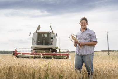 A man in a wheat field stands in front of a tractor