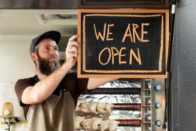 A Man holds a We Are Open sign as he opens his food truck for service